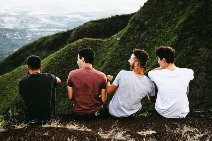 Four guys on a cliffside, laughing together at corny jokes.