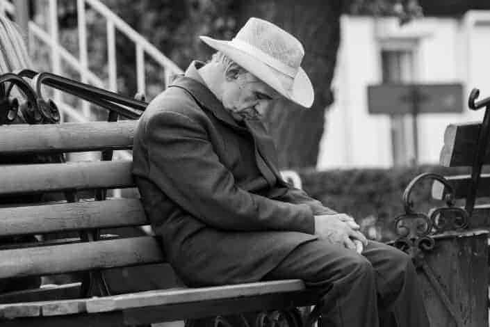 Old man fell asleep while sitting on a park bench.