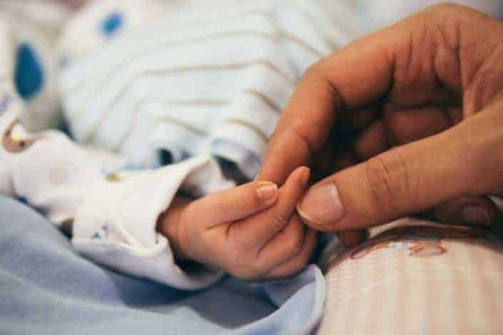 Adorable baby's hand touched by an adult's fingers.