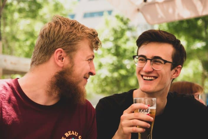 two men smiling at each other, the other holding a glass of beer